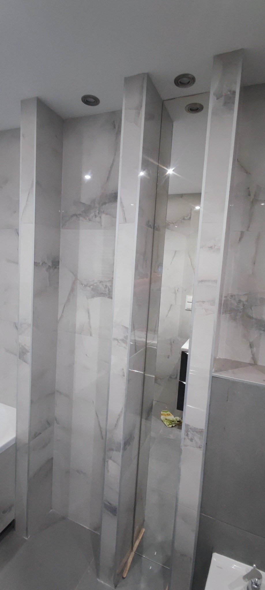 Nowoczesna łazienka z marmurowymi płytkami i lustrzanymi panelami pionowymi, widoczne odbicie wnętrza.