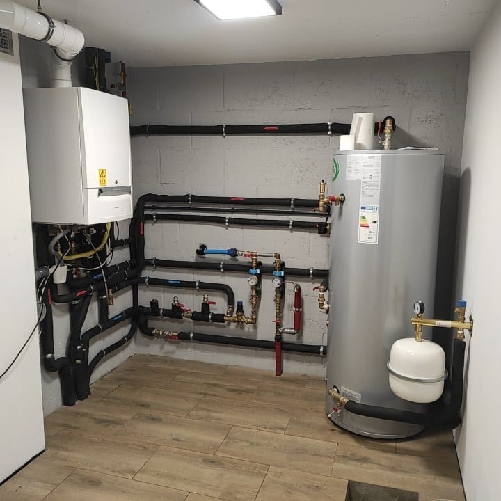 Zainstalowany piec gazowy z zasobnikiem ciepłej wody i rozbudowaną instalacją hydrauliczną w pomieszczeniu technicznym z drewnopodobną podłogą.