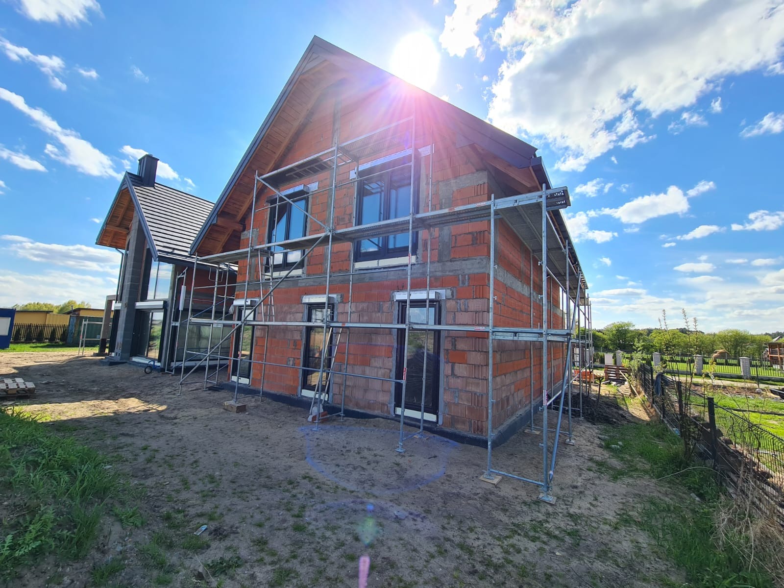 Dom w trakcie budowy z czerwonej cegły, otoczony rusztowaniem, widok z dołu w słoneczny dzień.