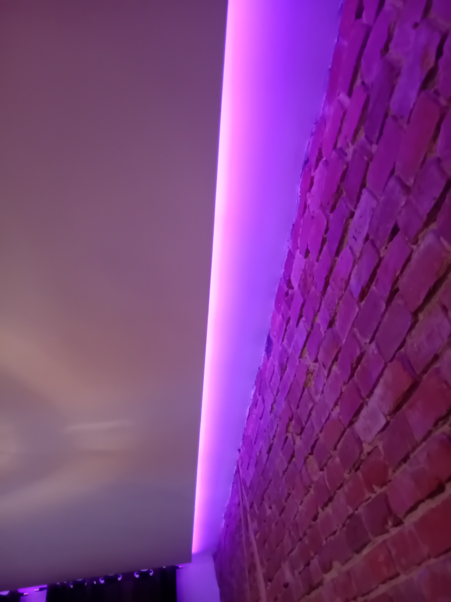 Ceglana ściana oświetlona fioletowym światłem LED przy suficie podwieszanym.