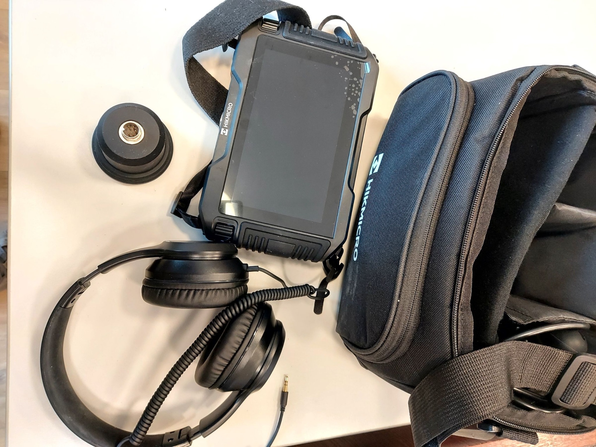 Geofon Hikmicro z akcesoriami: słuchawki, adapter i torba transportowa, leżące na jasnym podłożu.