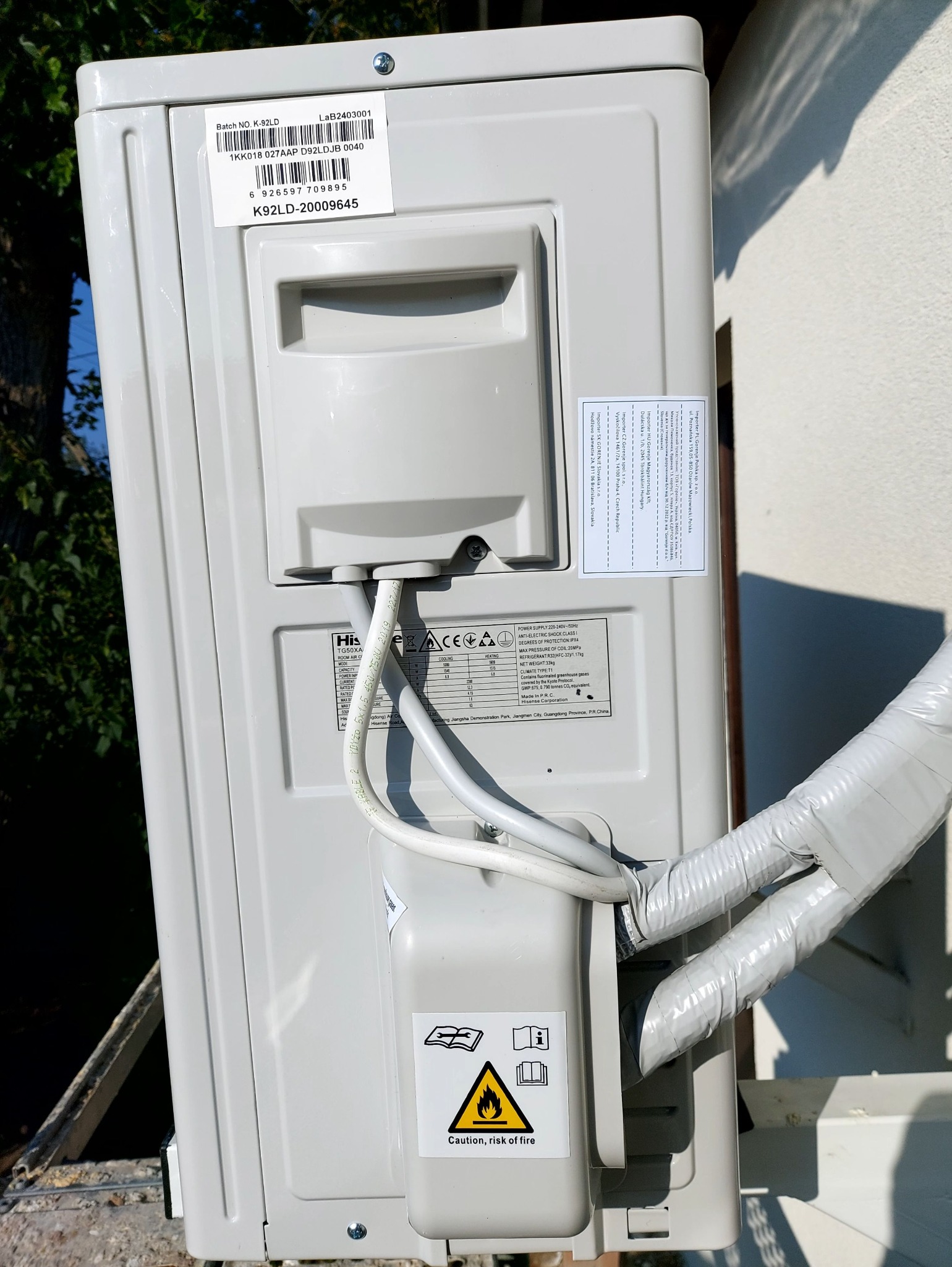 Zewnętrzna jednostka klimatyzacji Hisense z widocznymi przewodami w izolacji, tabliczką znamionową i ostrzeżeniem o ryzyku pożaru.