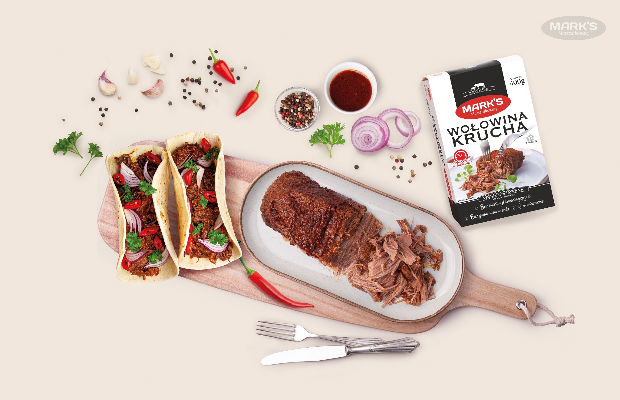 Delikatne mięso wołowe na owalnym talerzu, obok poszarpane mięso, dwie tortille z wołowiną, papryczkami chili i czerwoną cebulą, opakowanie wołowiny kruchej Mark's, czosnek, przyprawy i sos...