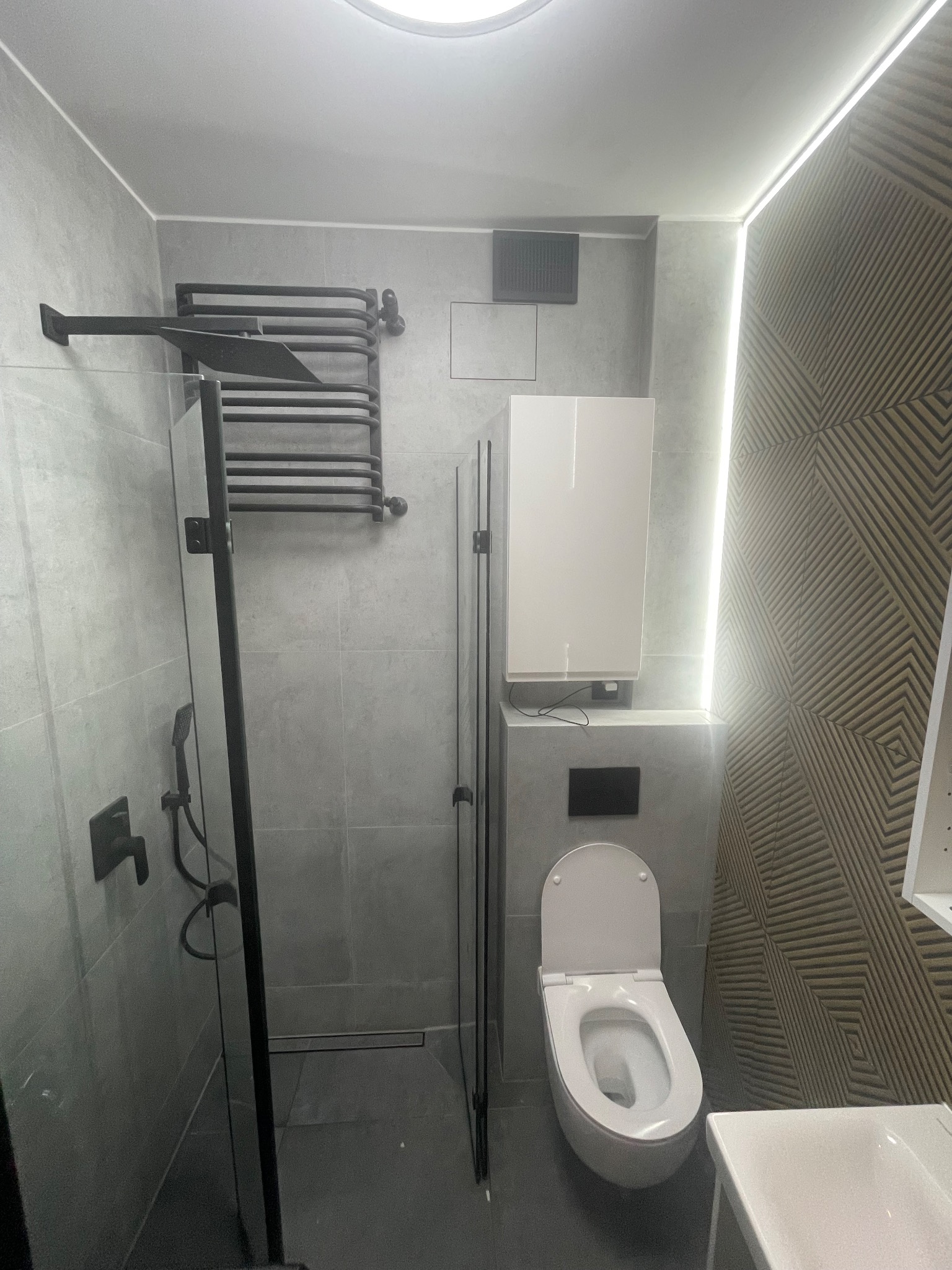 Nowoczesna łazienka z szarymi płytkami, czarną armaturą, kabiną prysznicową typu walk-in i dekoracyjną ścianą z podświetleniem LED.