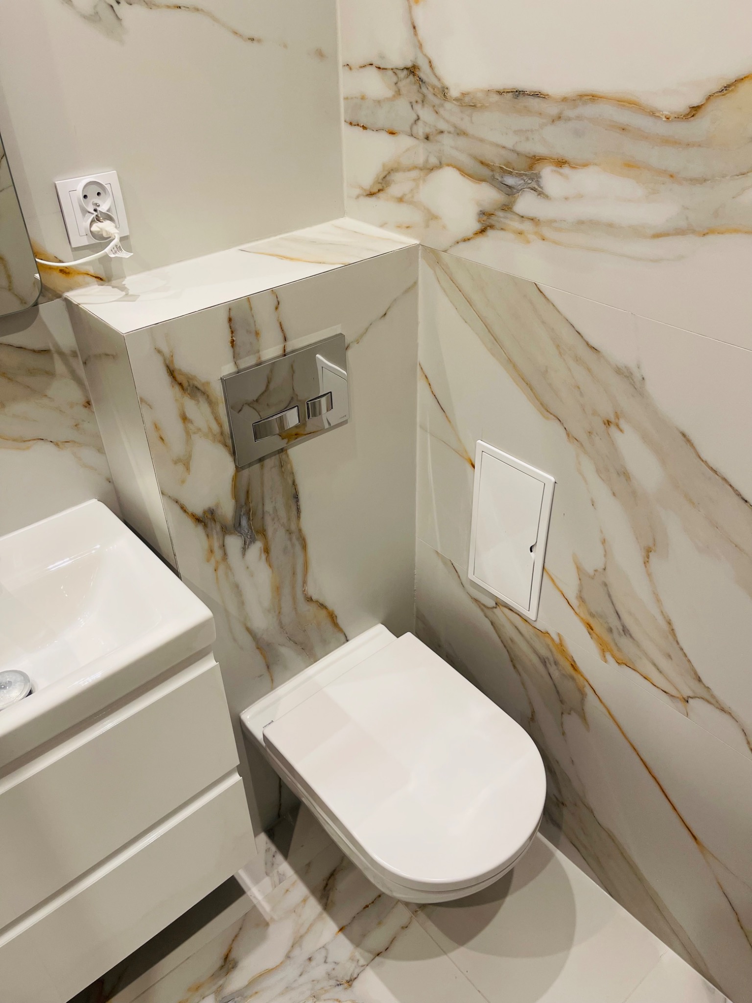 Elegancka łazienka w Chorzowie z marmurowymi płytkami, podwieszaną toaletą i białą umywalką z szafką. Nowoczesne wykończenie z dbałością o detale.