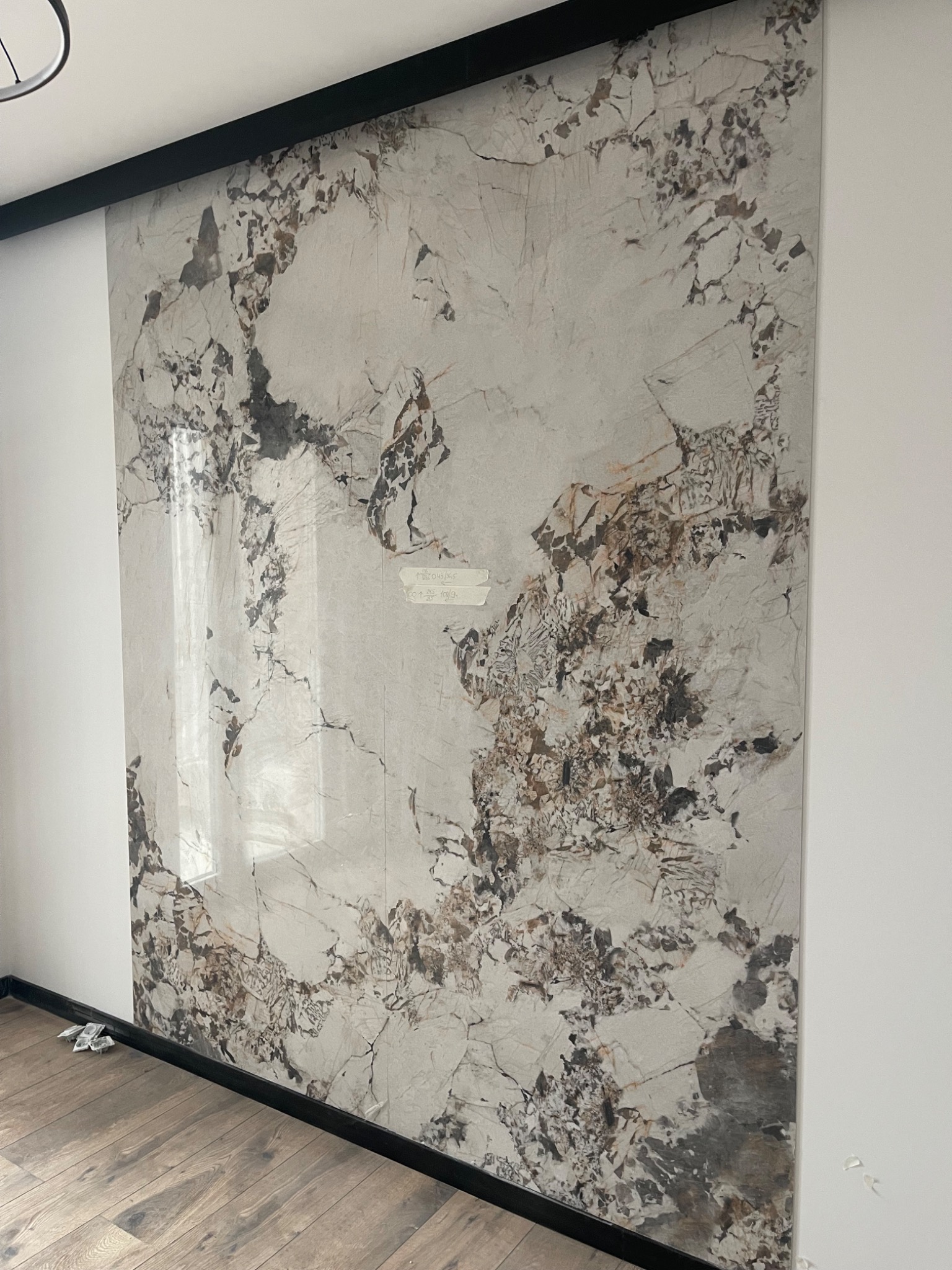 Ściana wykończona płytami imitującymi marmur, z widocznymi fugami i czarną listwą wykończeniową przy suficie i podłodze. Widoczna podłoga z paneli.