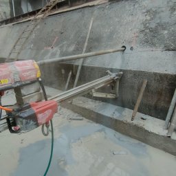 Technika diamentowa Diament JAKUB LIGUS - Wiertnica diamentowa Hilti DD 200-CA podczas wykonywania otworu w betonowej ścianie. Widoczne chłodzenie wodne i osprzęt montażowy.