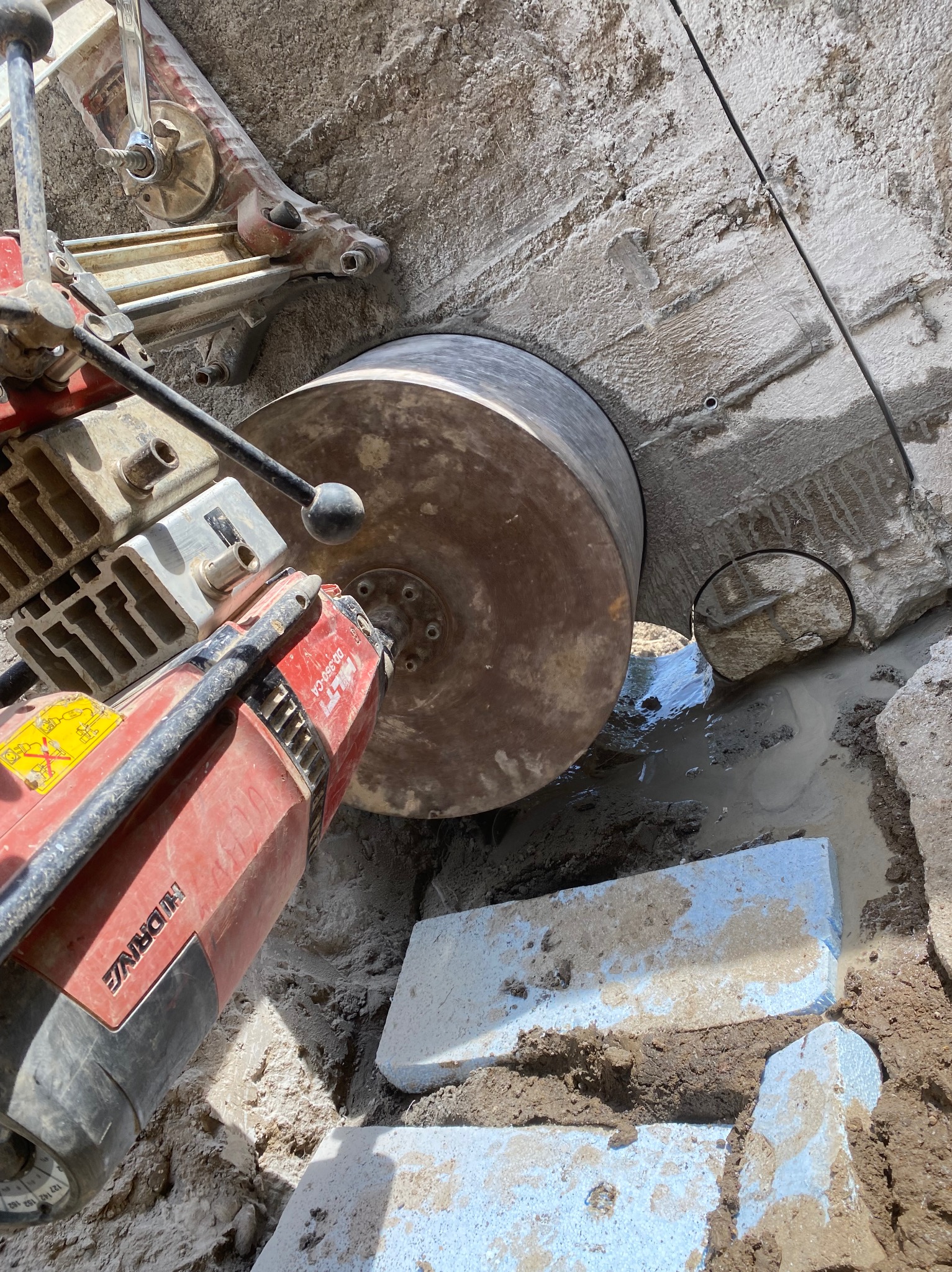 Wiertnica rdzeniowa Hilti DD 350-CA podczas wykonywania otworu w betonowej ścianie, widoczne chłodzenie wodne i fragment wyciętego rdzenia.
