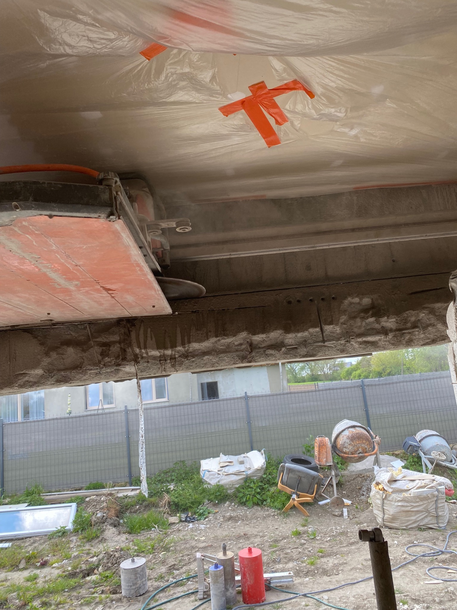 Cięcie żelbetowej konstrukcji stropu piłą diamentową z osłoną przeciwpyłową, widoczne zbrojenie i fragment ściany z zewnątrz budynku.