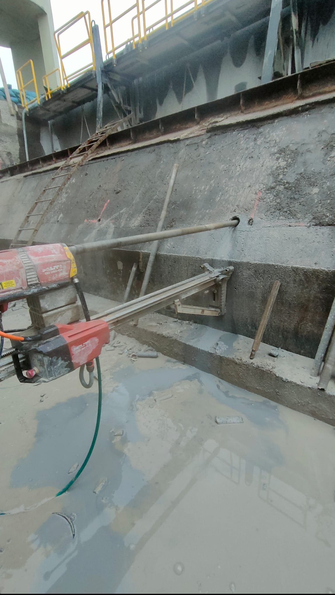Wiertnica diamentowa Hilti DD 200-CA podczas wykonywania otworu w betonowej ścianie. Widoczne chłodzenie wodne i osprzęt montażowy.
