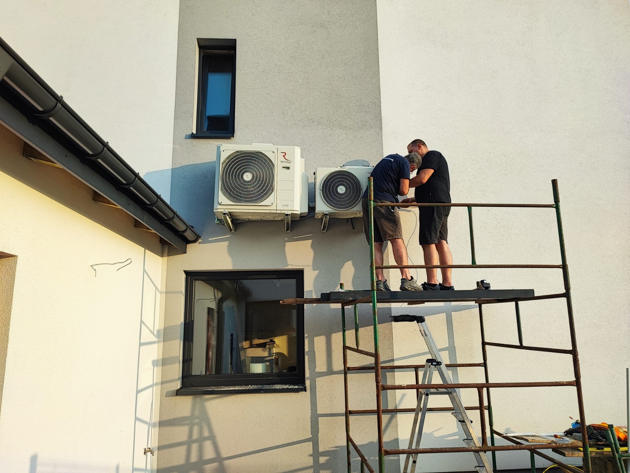 Montaż klimatyzacji na elewacji budynku przez dwóch monterów na rusztowaniu. Widoczne dwie jednostki zewnętrzne klimatyzatora marki Rotenso.