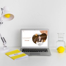 VisualSphere - Laptop wyświetla stronę internetową z portretem kobiety na tle biblioteki, obok lampka, notatnik 'Big Ideas', dzbanek z wodą i cytryna na białym biurku.