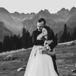 Zebra fotografia - Czarno-białe zdjęcie nowożeńców w objęciach na tle górskiego krajobrazu z lasem iglastym i mglistymi szczytami.