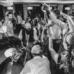 Zebra fotografia - Czarno-białe zdjęcie z góry przedstawiające grupę gości weselnych otaczających parę młodą podczas oczepin w sali bankietowej.