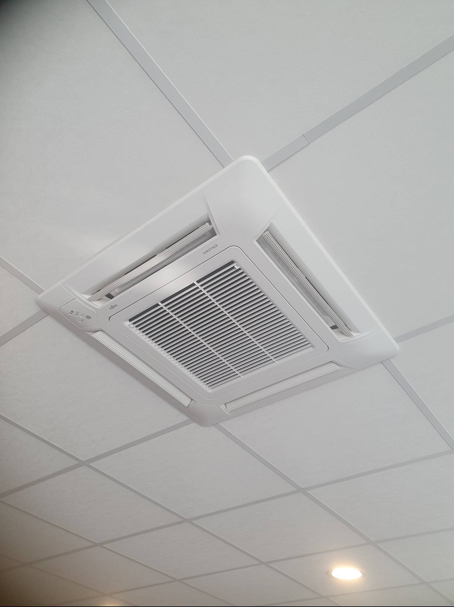 Biała, kasetonowa klimatyzacja sufitowa Fujitsu Airstage w biurze, widok od dołu pod kątem.
