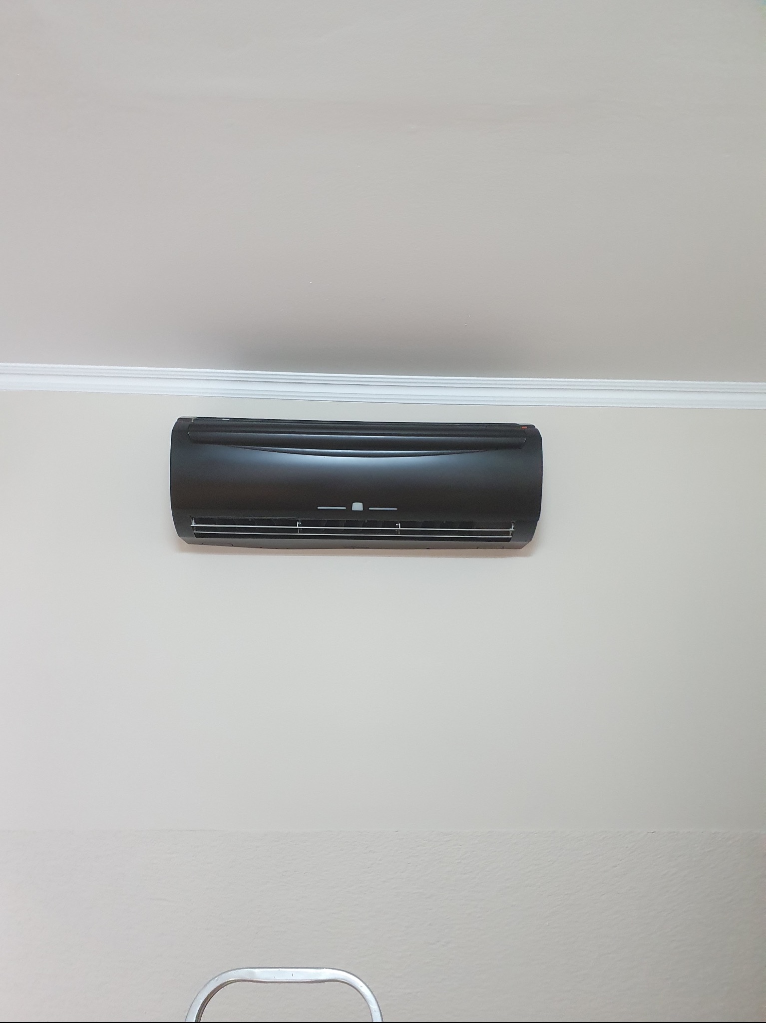 Czarny klimatyzator ścienny zamontowany w pomieszczeniu o jasnych ścianach, widoczny fragment drabiny.