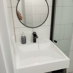 INSTAL-BUD - Nowoczesna łazienka z białą umywalką nablatową, czarną armaturą i dekoracyjnym okrągłym lustrem nad pralką automatyczną.