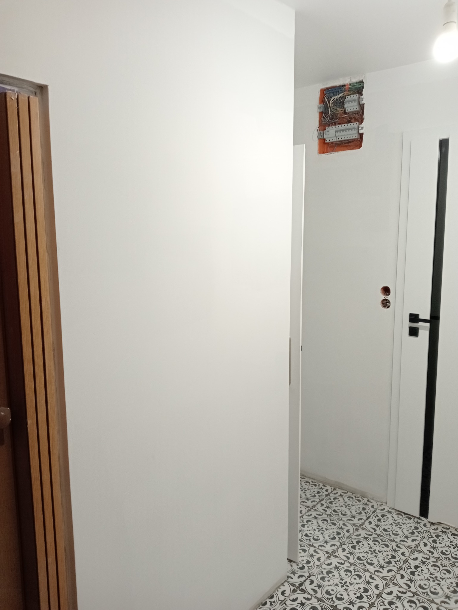 Nowe, wzorzyste płytki podłogowe w korytarzu z otwartą skrzynką elektryczną na ścianie i dwiema parami drzwi.