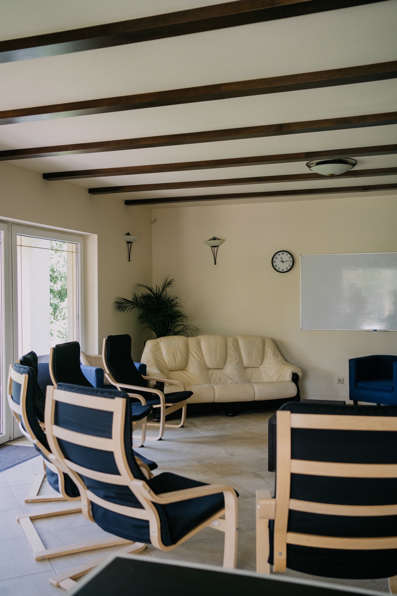 Jasne wnętrze sali terapeutycznej z krzesłami ustawionymi w kręgu, kremową sofą i białą tablicą, przygotowane do sesji grupowej terapii uzależnień.