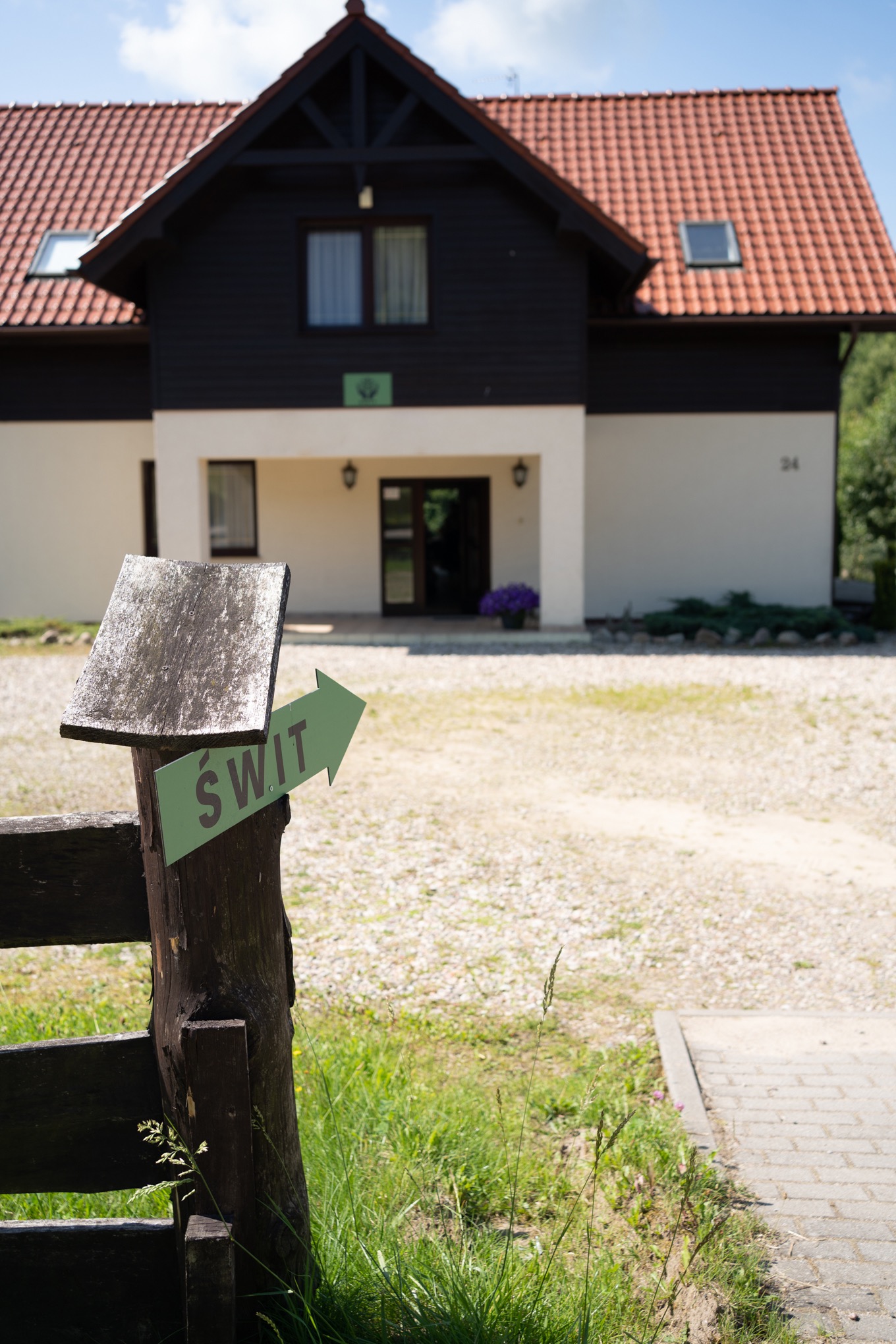 Budynek ośrodka z drewnianą konstrukcją i czerwoną dachówką, zielony drogowskaz z napisem 'ŚWIT' na pierwszym planie.