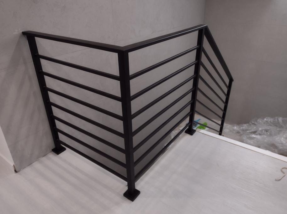 Nowoczesna balustrada schodowa z czarnych, poziomych profili na szarym tle ściany i białych stopni schodów.