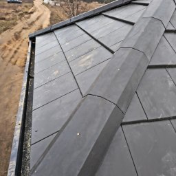 MkDach - Nowoczesny dach pokryty czarną dachówką ceramiczną, widok z góry na kalenicę i rynnę, w tle polna droga i drzewa.