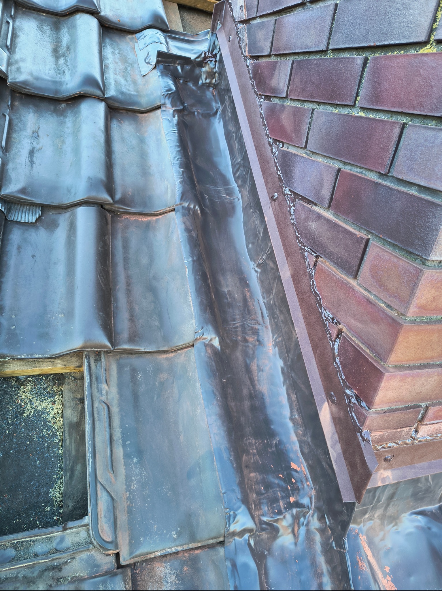 Fragment połaci dachu z brązową dachówką ceramiczną i metalową obróbką blacharską, widoczne detale łączeń i zabezpieczeń przeciwwodnych.