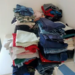 Stosy poskładanych ubrań w różnych kolorach i wzorach, w tym dżinsy, koszulki i flanelowe koszule, ułożone na białej półce.