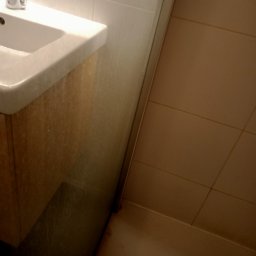 Perfekcyjna Pani Domu - Umywalka z szafką w łazience, widoczne zabrudzenia i zacieki na powierzchni umywalki i szafki oraz na ścianie wyłożonej płytkami.