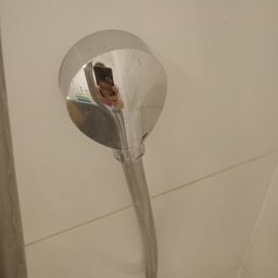 Perfekcyjna Pani Domu - Błyszcząca słuchawka prysznicowa zamontowana na kafelkowej ścianie, z widocznym odbiciem osoby robiącej zdjęcie telefonem.