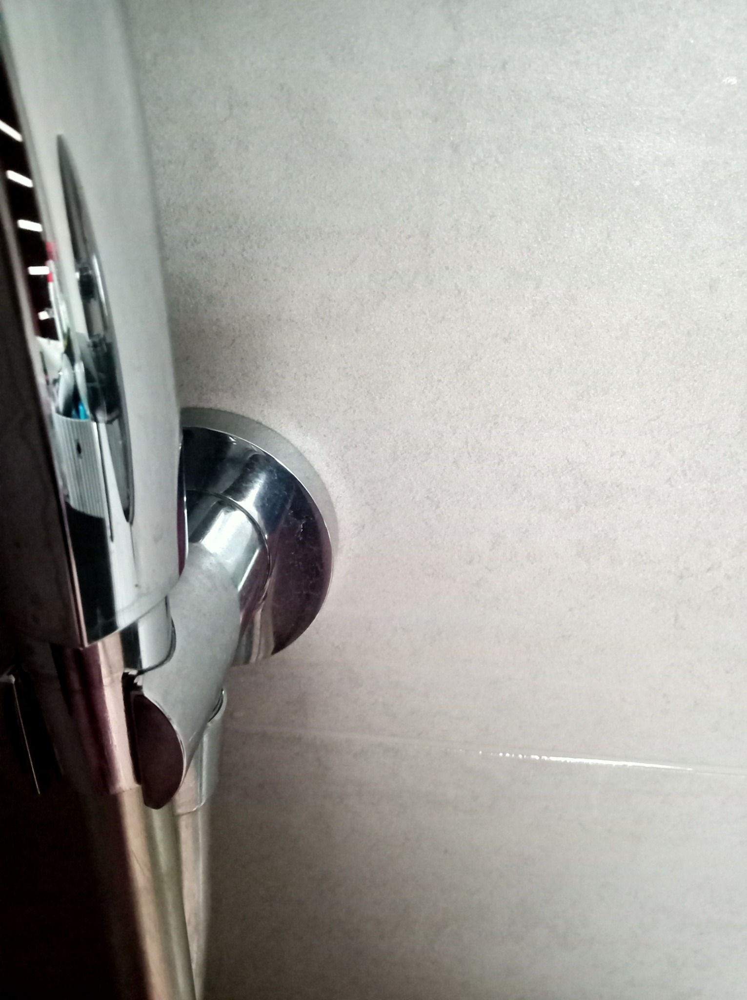 Błyszcząca, chromowana słuchawka prysznicowa zamontowana na ścianie z jasnych, matowych płytek.