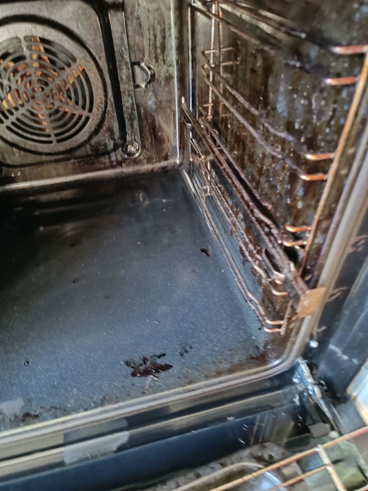 Wnętrze bardzo zabrudzonego piekarnika z przypalonymi resztkami jedzenia na dnie i ściankach, widoczne metalowe ruszty z osadami.