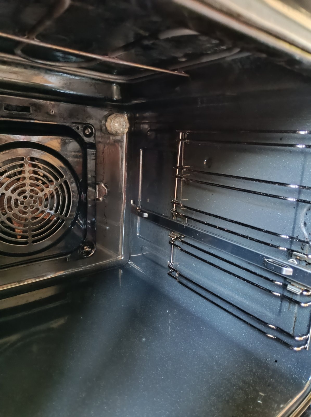 Wnętrze brudnego piekarnika przed czyszczeniem, widoczny wentylator, prowadnice i przypalenia.