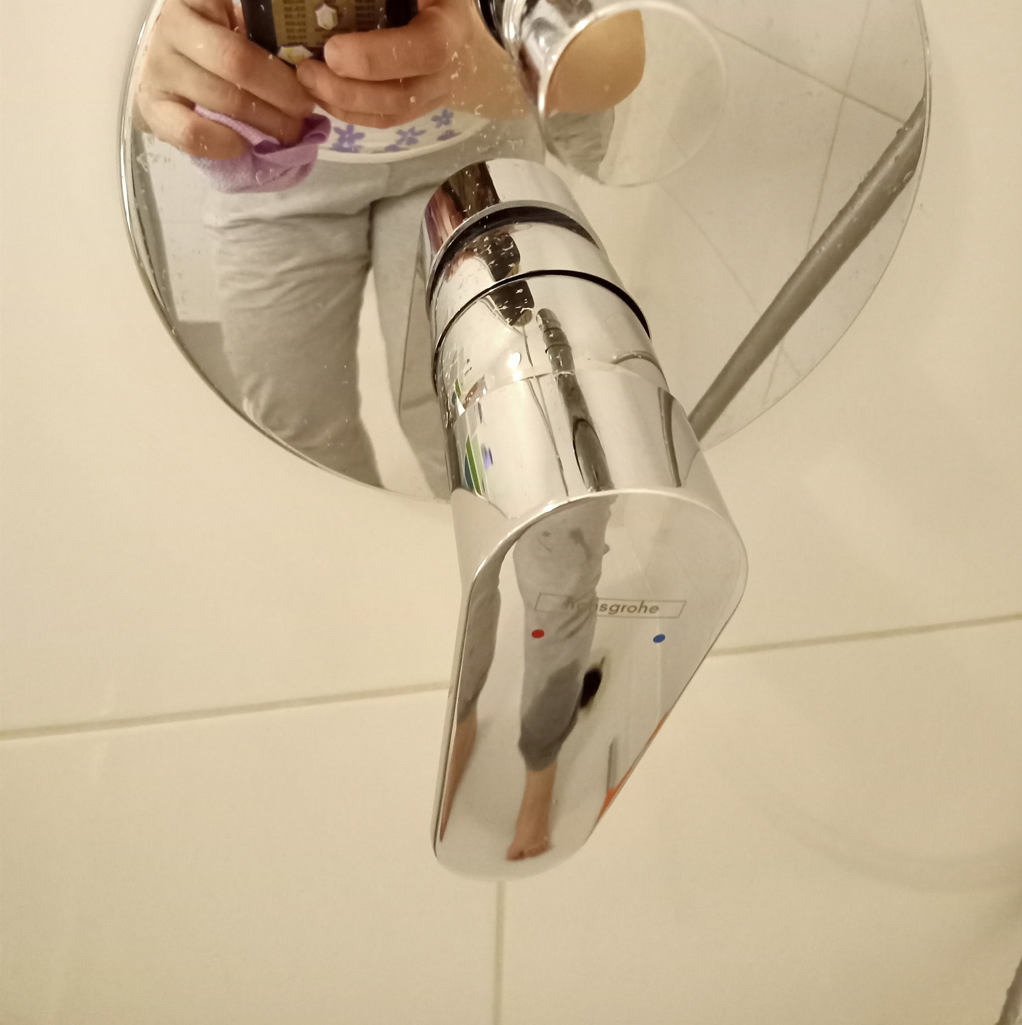 Błyszcząca bateria umywalkowa marki Hansgrohe, czyszczona fioletową ściereczką, widoczne odbicie osoby robiącej zdjęcie.