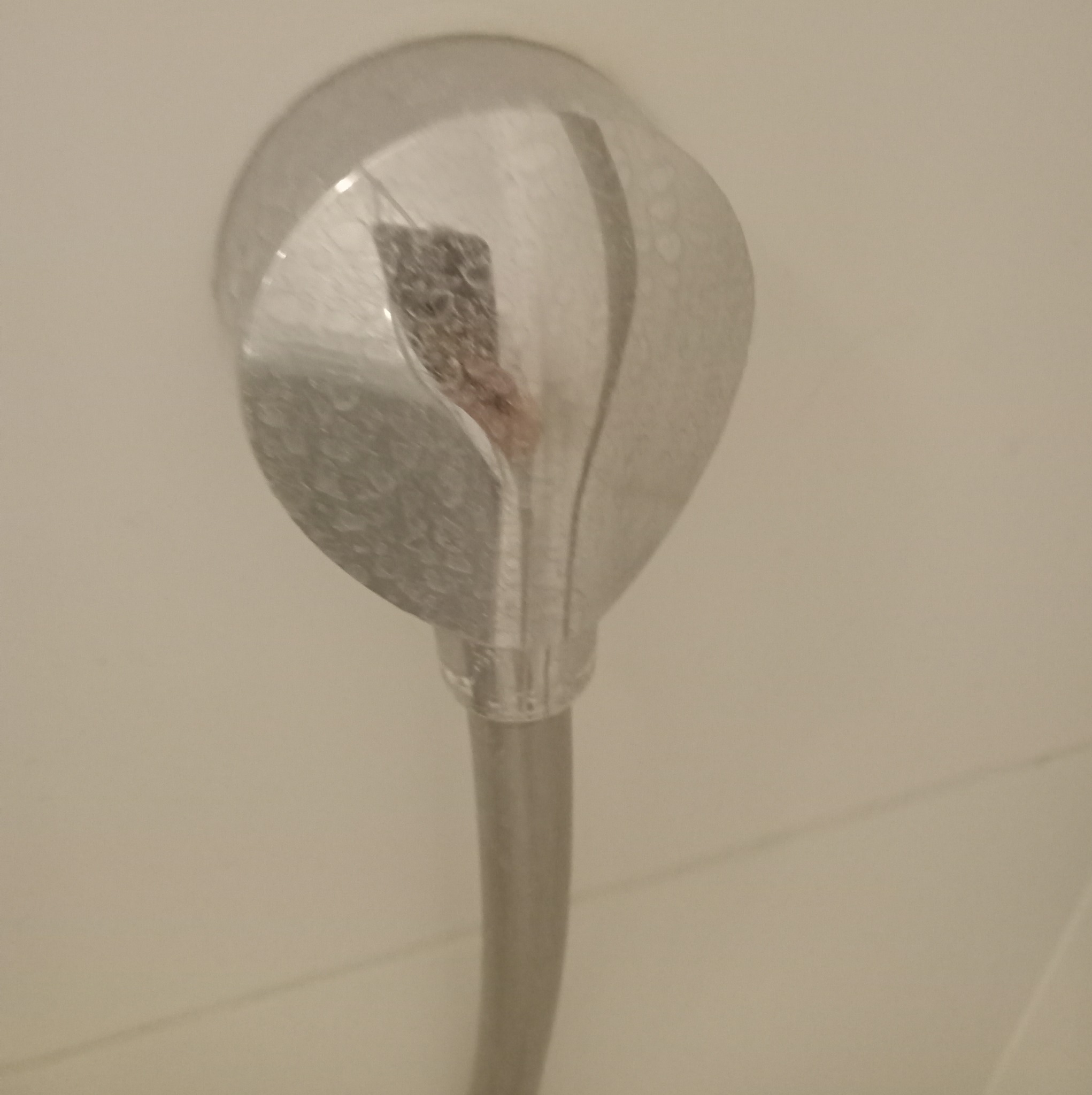 Metalowa słuchawka prysznicowa z widocznymi śladami osadu wewnątrz, zamontowana na białej ścianie.