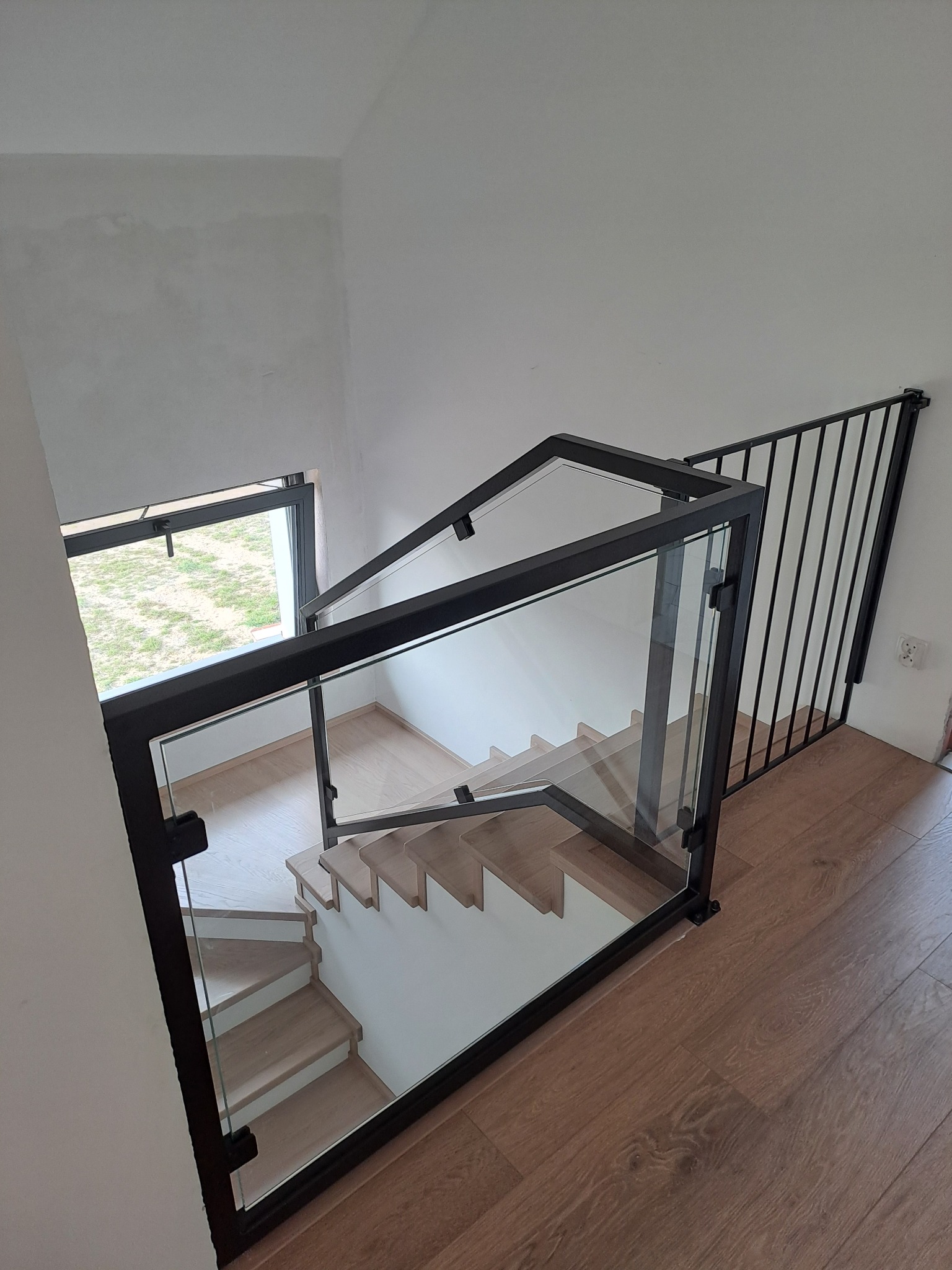 Nowoczesna balustrada szklana ze stalowymi elementami w czarnym kolorze, zamontowana na schodach wewnątrz budynku, widok z góry.