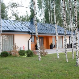GES GROUP SPÓŁKA Z OGRANICZONĄ ODPOWIEDZIALNOŚCIĄ - Nowoczesny dom jednorodzinny z szarą blachą na dachu, elewacją z elementami drewnianymi i białymi ścianami, otoczony młodymi brzózkami i trawnikiem.