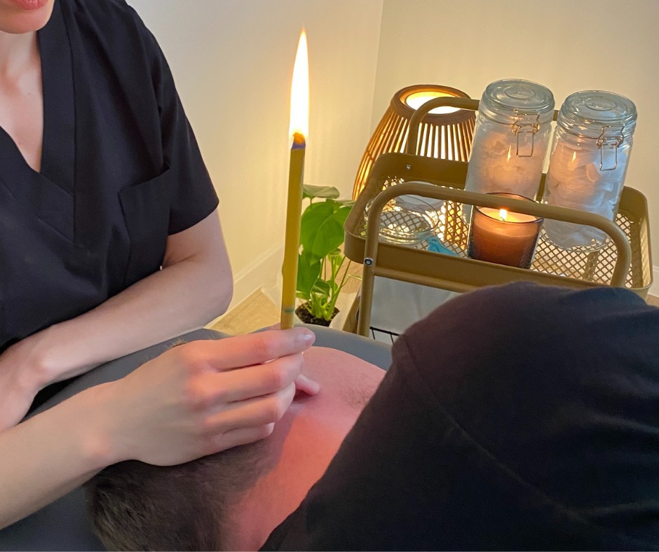 Zabieg świecowania uszu: płonąca świeca konchowa w uchu pacjenta, w tle wózek z akcesoriami, lampa i roślina doniczkowa.