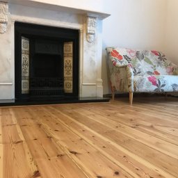 Cyklinomania.pl - Jasna, odnowiona podłoga z desek w pokoju z marmurowym kominkiem i sofą w kwiaty.