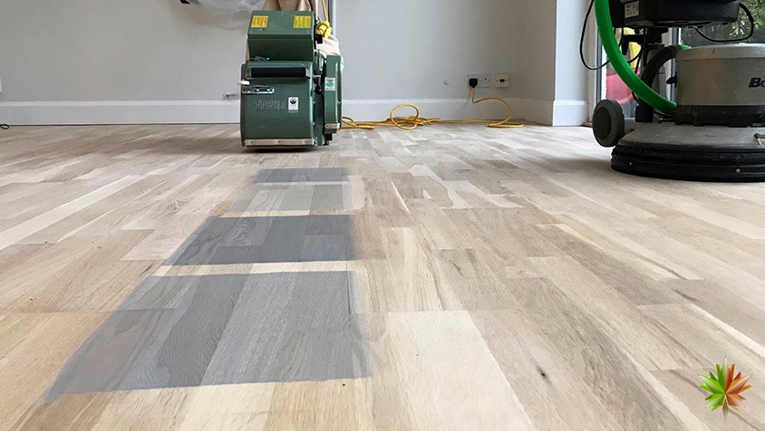 Parkiet z jasnego drewna w trakcie renowacji, widoczne ślady po szlifowaniu i maszyny do cyklinowania.