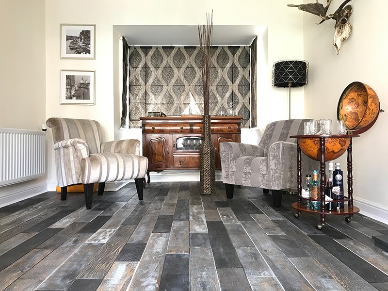 Salon z szarymi panelami podłogowymi w stylu rustykalnym, dwoma fotelami w paski, komodą i dekoracjami.