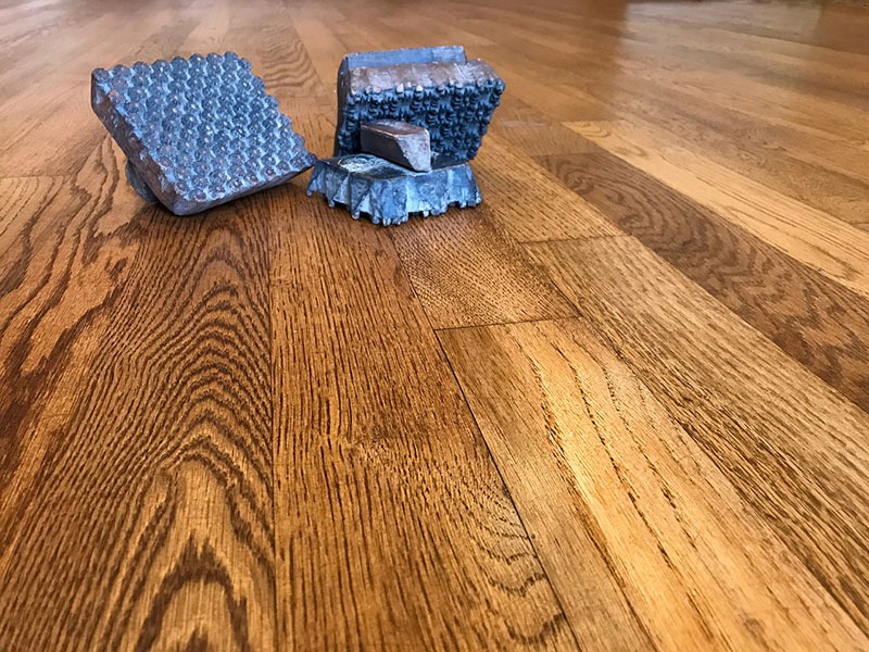 Polakierowana podłoga z desek dębowych z widocznym usłojeniem i fakturą drewna, na której leżą trzy metalowe stempelki z wypukłymi wzorami.