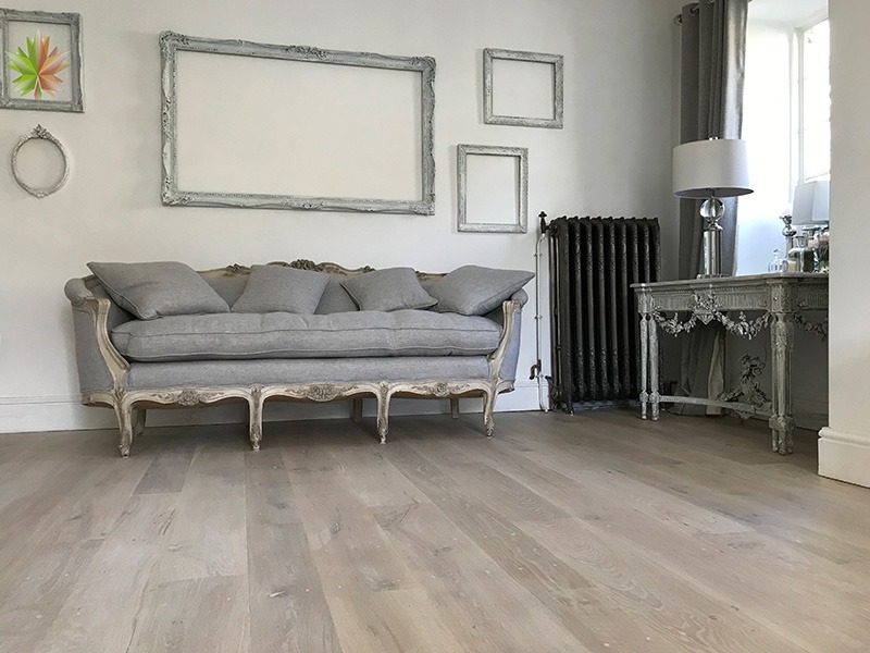 Jasna, szczotkowana podłoga drewniana w salonie z szarą sofą Ludwika i ozdobnymi ramami na ścianie.