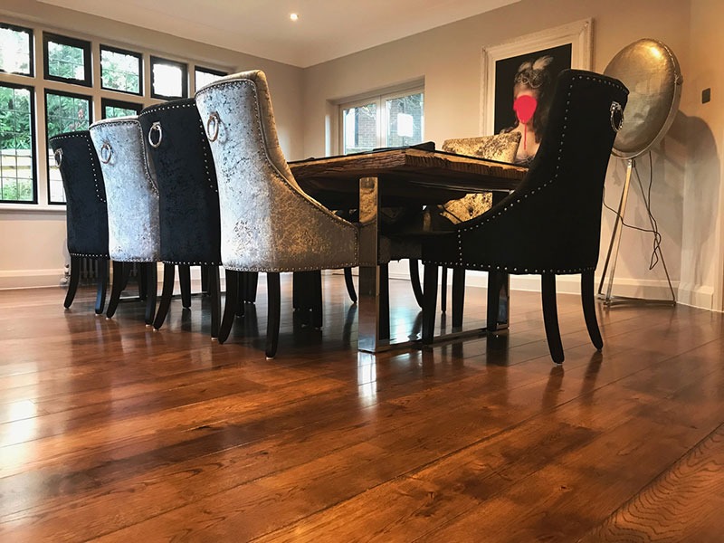 Błyszcząca, lakierowana podłoga drewniana w jadalni z krzesłami tapicerowanymi welurem w odcieniach szarości i czerni, widoczne detale wykończenia podłogi przy ścianie.