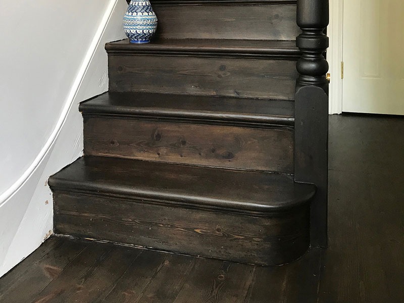 Ciemne, drewniane schody po renowacji, z widoczną strukturą drewna i dekoracyjnym wazonem na górnym stopniu.