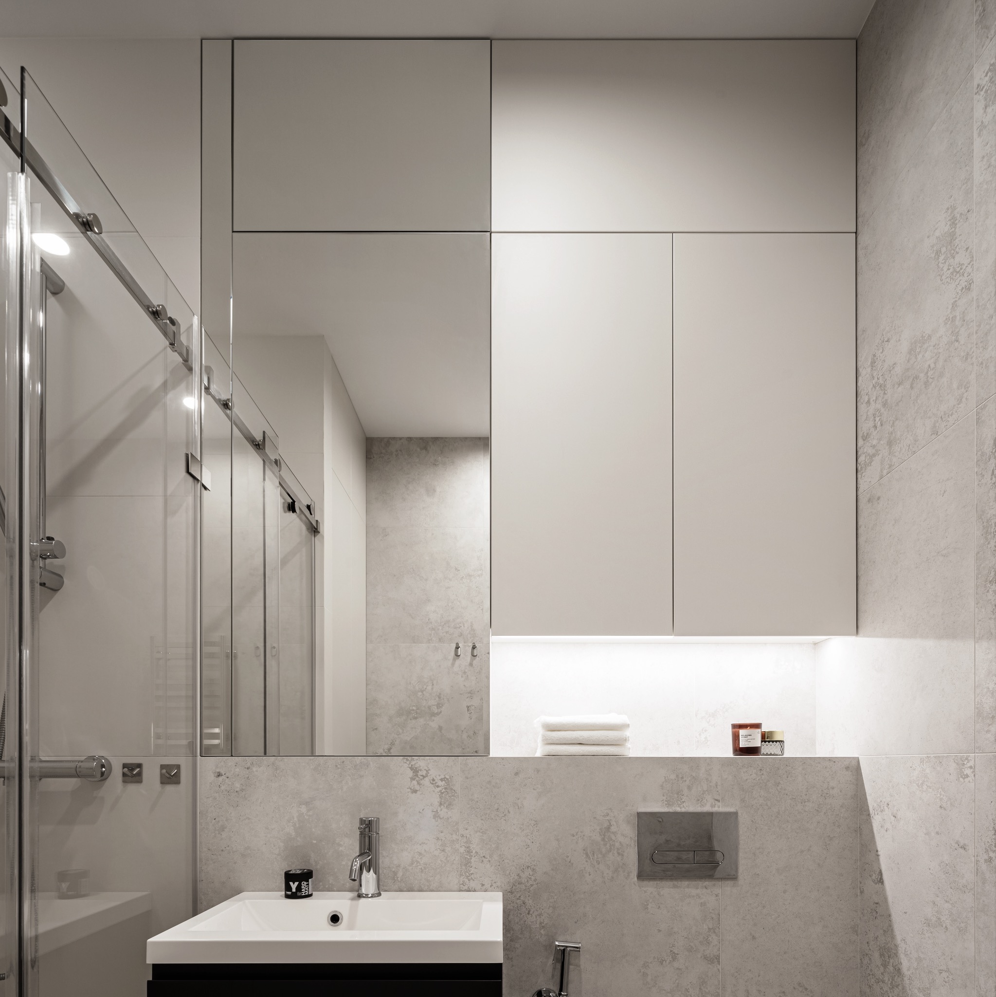 Nowoczesna łazienka z kabiną prysznicową przesuwną, umywalką nablatową, szafkami wiszącymi z oświetleniem LED i szarą płytką imitującą beton.