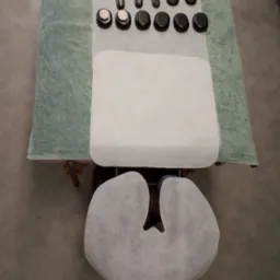 Przygotowany stół do zabiegu z kamieniami bazaltowymi różnej wielkości, ułożonymi w rzędach na zielonym ręczniku, z podkładem pod głowę.