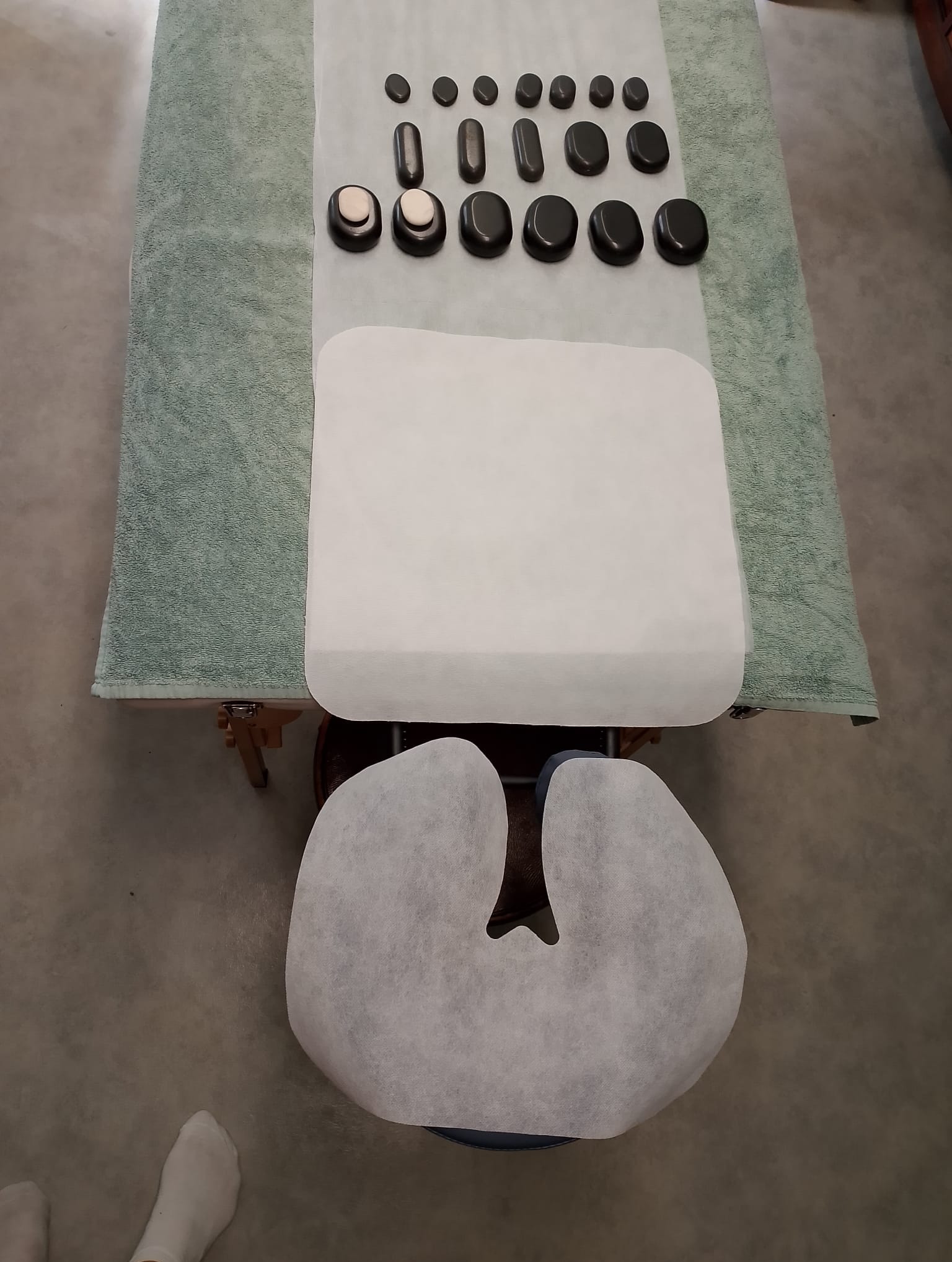 Przygotowany stół do zabiegu z kamieniami bazaltowymi różnej wielkości, ułożonymi w rzędach na zielonym ręczniku, z podkładem pod głowę.