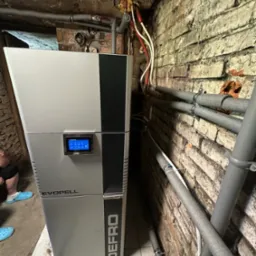 Nowoczesny piec DEFRO EVOPELL z dotykowym panelem sterowania, zainstalowany w piwnicy z odsłoniętą cegłą i rurami grzewczymi.