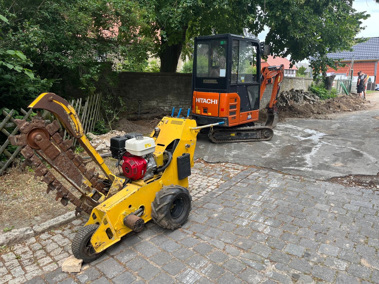Żółta koparka łańcuchowa z czerwonym silnikiem Honda i pomarańczowa mini koparka Hitachi na brukowanej ulicy, przygotowane do prac ziemnych.